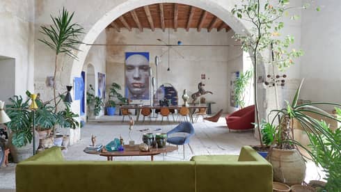 Large room with tropical plants, contemporary furnishings, an arched stone wall and artwork in the distance