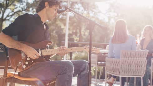 Man plays electric guitar at microphone on sunny patio