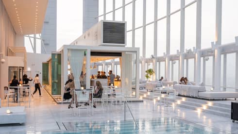 People mingle around a contemporary white bar next to pool