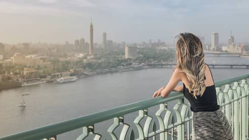 Woman with long blonde hair standing on balcony overlooking Nile River and Cairo