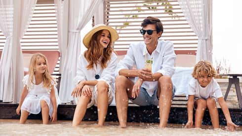 Man, woman and two kids sit on cabana deck with feet in the water