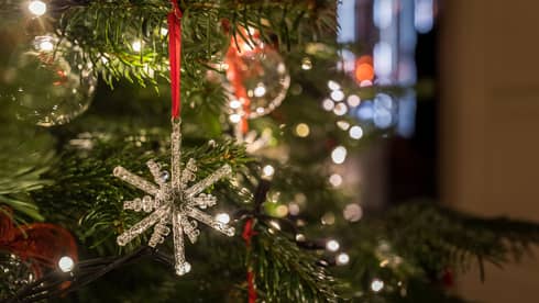 Close-up of a crystal snowflake ornament hanging on a Christmas tree with festive lights in the background