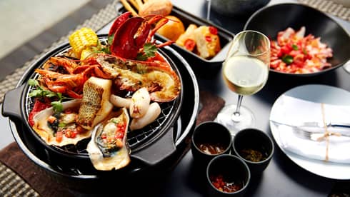 Grilled fish, oysters, lobster, crab on grill plate next to white wine, garnishes