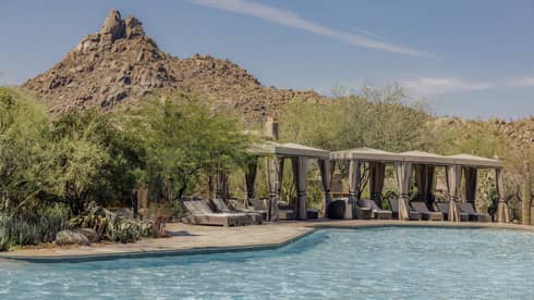 Pool with cabanas that have lounge chairs with a backdrop of the mountains.
