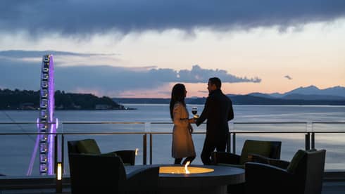 A couple holds hands and shares wine on the balcony as the sun sets