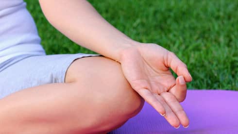 Side of hand, leg in cross legged meditation pose on yoga mat 