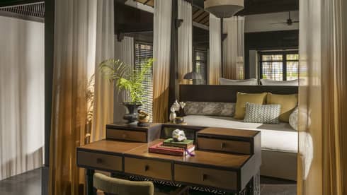 Interior of a private villa at a resort, with sheer curtains outlining a four-post king bed, and a wooden table at the foot of the bed