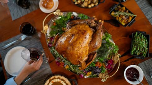 A table with a cooked turkey and Thanksgiving sides around it.