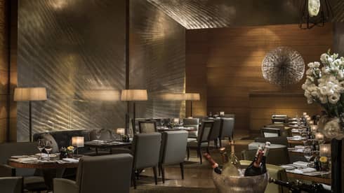 Elegant restaurant dining area with softly lit tables, upholstered chairs, and ambient lighting, set for a formal dinner service.