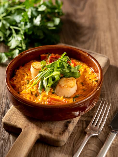 Scallops plated over Italian Carnaroli rice with tomato sauce and garnished with rocket greens