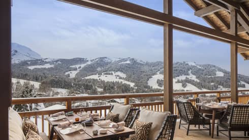 Dining tables, chairs, cushions under wood roof looking over snow-covered mountains