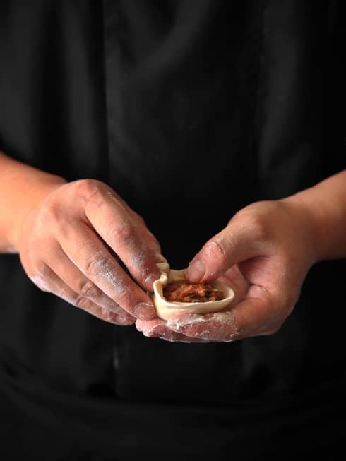 A close up of hands holding a small dough crust with a red sauce inside