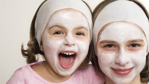 Two smiling children wearing headbands and facial masks, one laughing joyfully, showcasing a fun skincare moment.