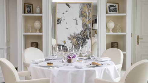 Formally set white round dining table with vertical art and display shelves in backdrop