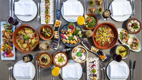 Overhead view of a table filled with a variety of Ramadan dishes along with six white plates and sets of cutlery