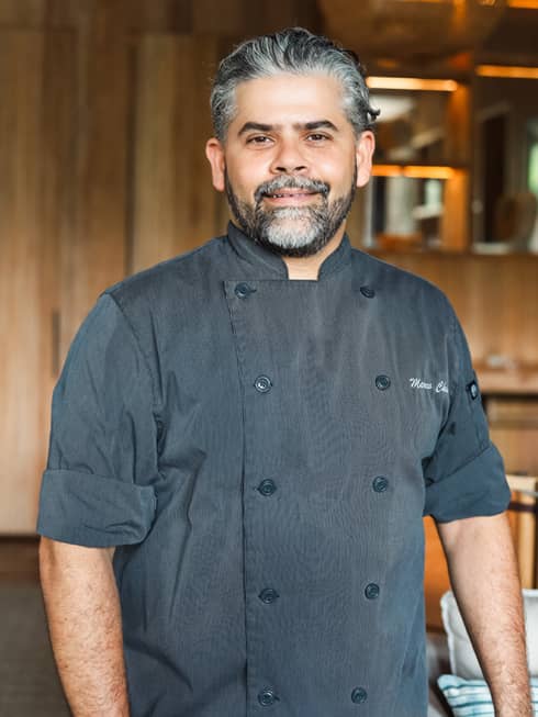 A male chef in a grey chef's coat in a wood paneled room.