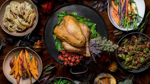 An aerial view of a Thanksgiving dinning table with turkey, sliced sweet potatoes, and a variety of roasted and fresh vegetables 