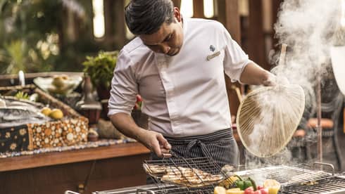 Ikan Ikan chef fans hot food over a grill with fresh peppers