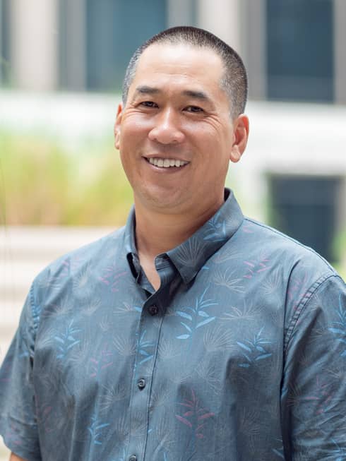 Smiling person in blue patterned button-down shirt poses for a headshot