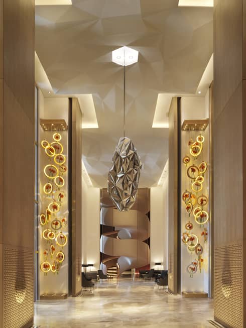 A paper mache installation that looks like a minimal bees hive hangs from the ceiling in a neutral lobby corridor