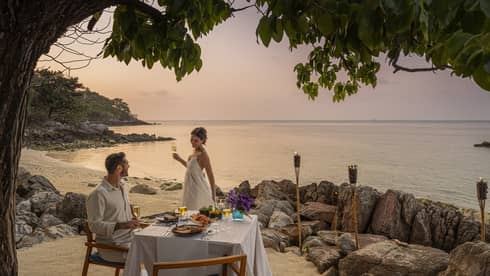 A beach dinner date at dusk, with a couple enjoying a serene seaside view.