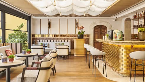 A well lit dining outlet with white chairs, large windows and a gold bar.