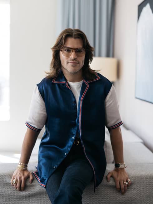A man with long hair, a blue vest jacket and tinted glasses.