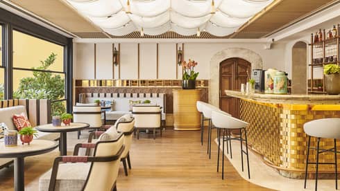 A well lit dining outlet with white chairs, large windows and a gold bar.