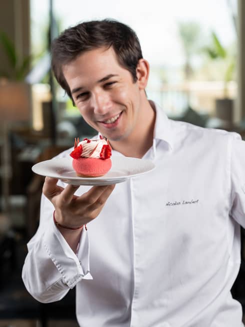 Chef Lambert in a white Four Seasons shirt, holding a red pastry.