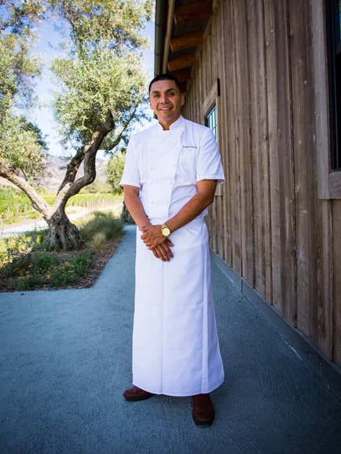 A chef in a long chefs coat standing outside.