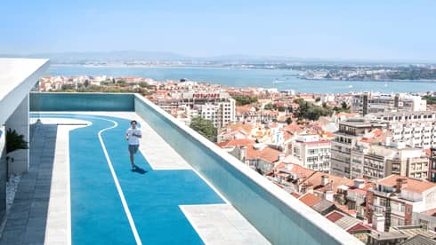 Man running on rooftop track, Lisbon city rooftops below