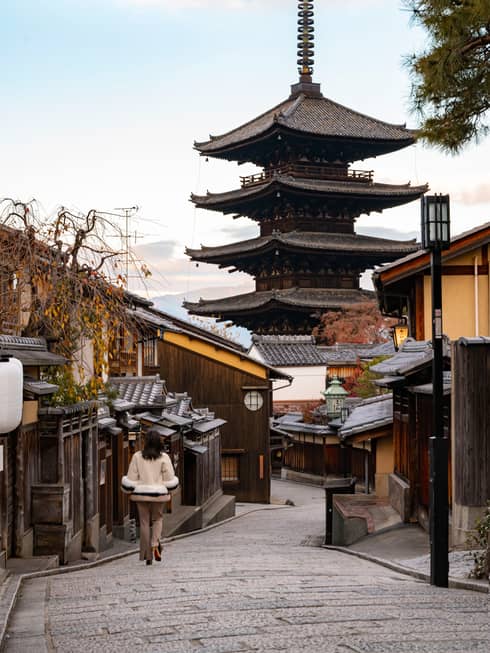 Woman walks down cobblestone street in Kyoto towards Japanese pagoda