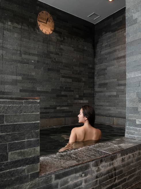Female guest soaks in the grey stone onsen bath