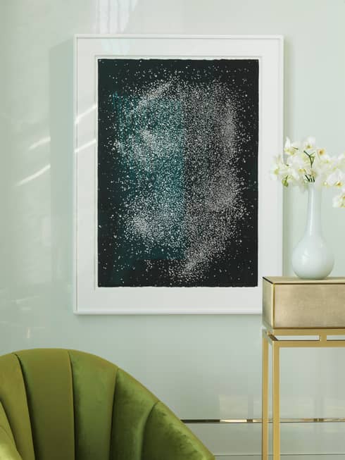 Close-up of green chair and jewel-toned painting on black with white frame against white wall