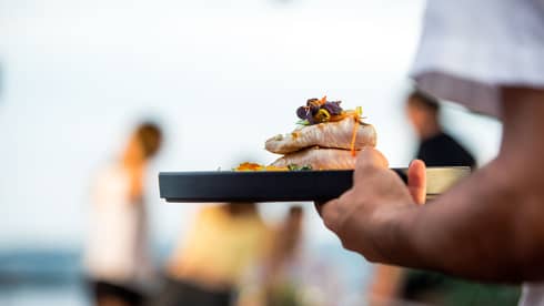 Close-up of server carrying tray with two thick, grilled fish fillets with edible flower garnish