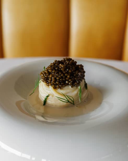 Artfully plated roll of past topped with caviar in a white bowl