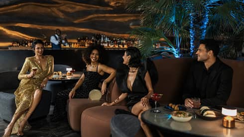 Three women and one man mingle over cocktails at Dubai hotel rooftop lounge