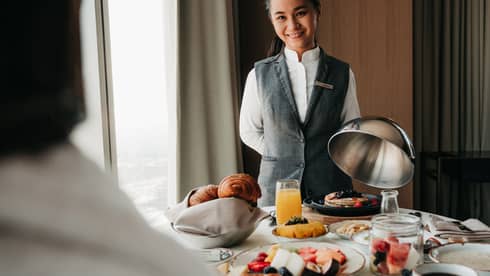 Smiling team member serving an elaborate breakfast spread in a guest room at Four Seasons Hotel Kuwait.