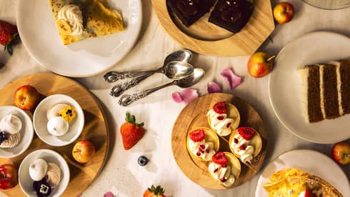 An arrangement of small plates with brunch food items on a tabletop, along with scattered fruits and flower petals