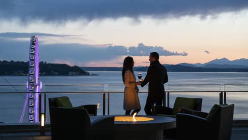 A couple holds hands and shares wine on the balcony as the sun sets