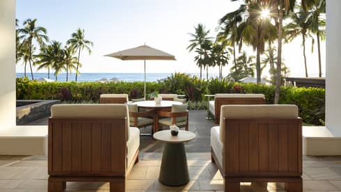 Contemporary private outdoor terrace of a resort suite, with dining table and lounge chairs facing palm trees and ocean