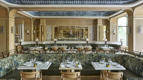 Bright, open restaurant space with neutral-coloured walls, decorative recessed ceilings, natural light, and tables and chairs and banquette seating