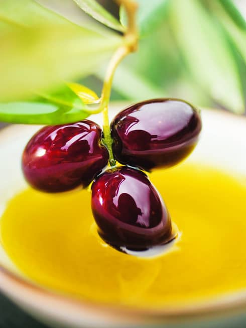 Close-up of three shiny purple olives on vine over yellow sauce