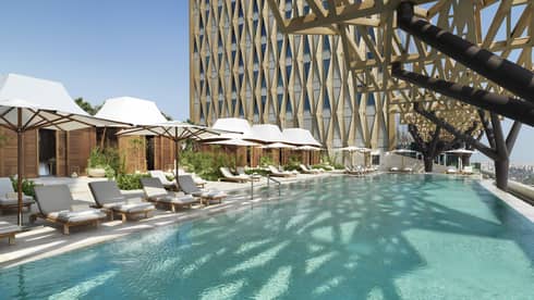 An olympic size pool surrounded by lounge chairs shaded by large white umbrellas