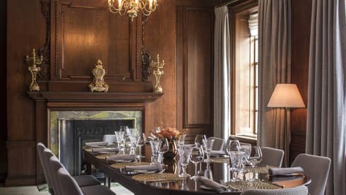 Private dining table in meeting room with wood walls, elegant fireplace, tall sunny windows