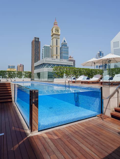 Glass-walled pool on a rooftop deck with skyscrapers in the background