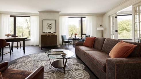 Bright State Suite living room with long rustic red sofa, small glass table, swirl rug, retro-style bar and dining cafe table