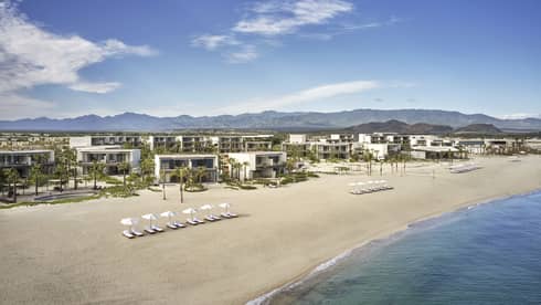 A beach with building and lounge chairs.