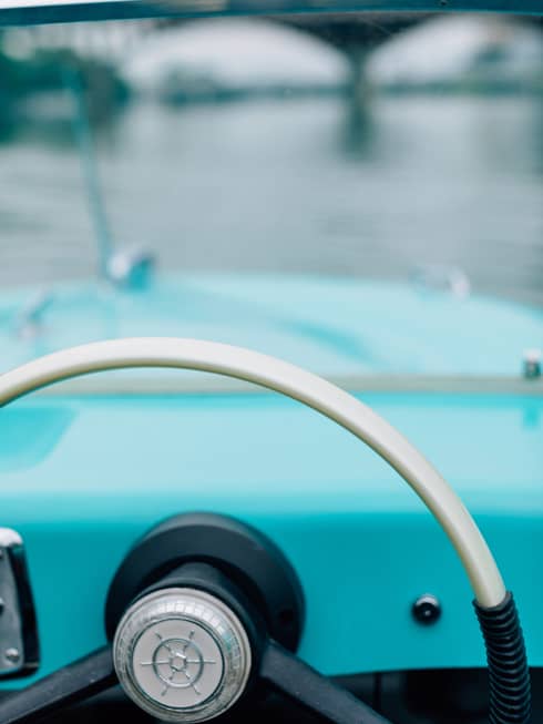 The steering wheel of an old boat with a bridge in the distance.