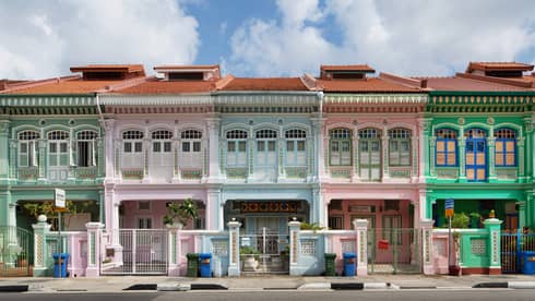 A wide shot of four residential buildings lined up like a rainbow – green, pink and blue with red terracotta roofs. 